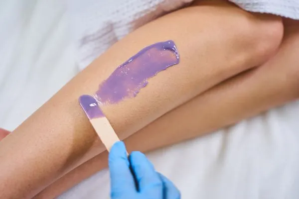 Esthetician applying warm wax to a guest's leg during a professional waxing service
