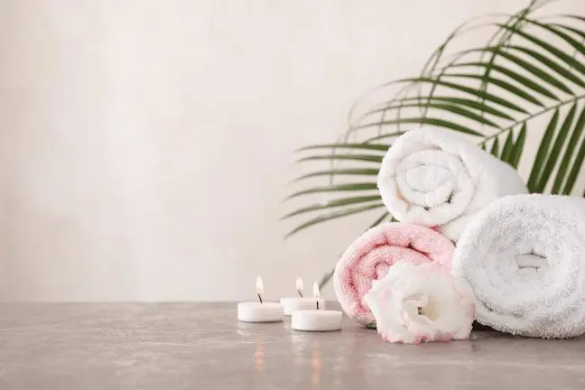 Rolled spa towels, lit candles, and a flower arranged on a grey surface